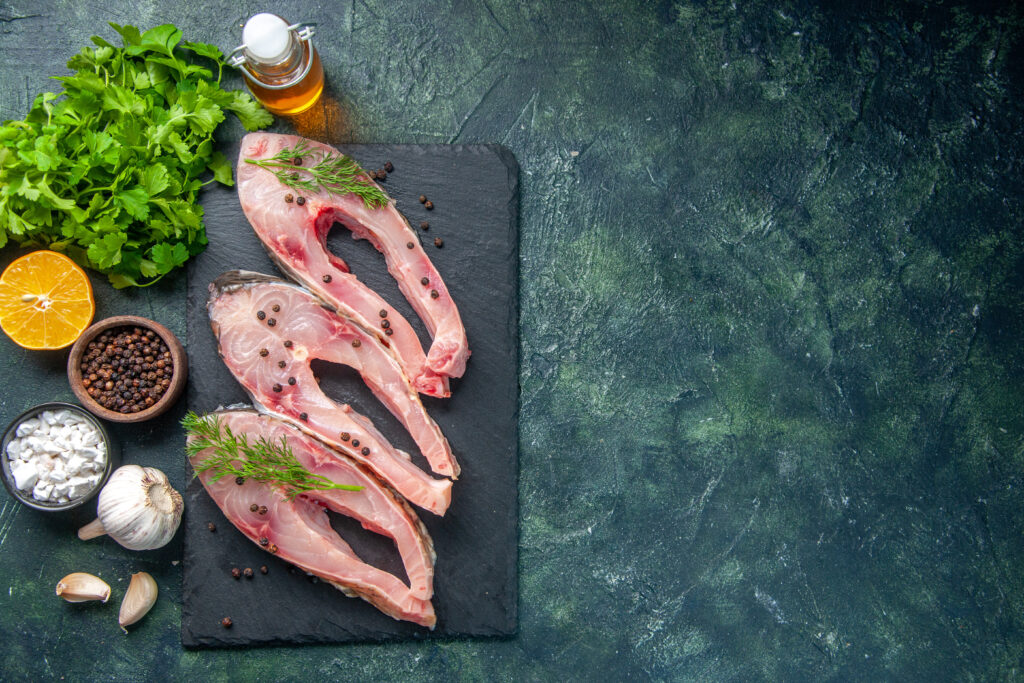 About top view fresh fish slices with greens dark blue background