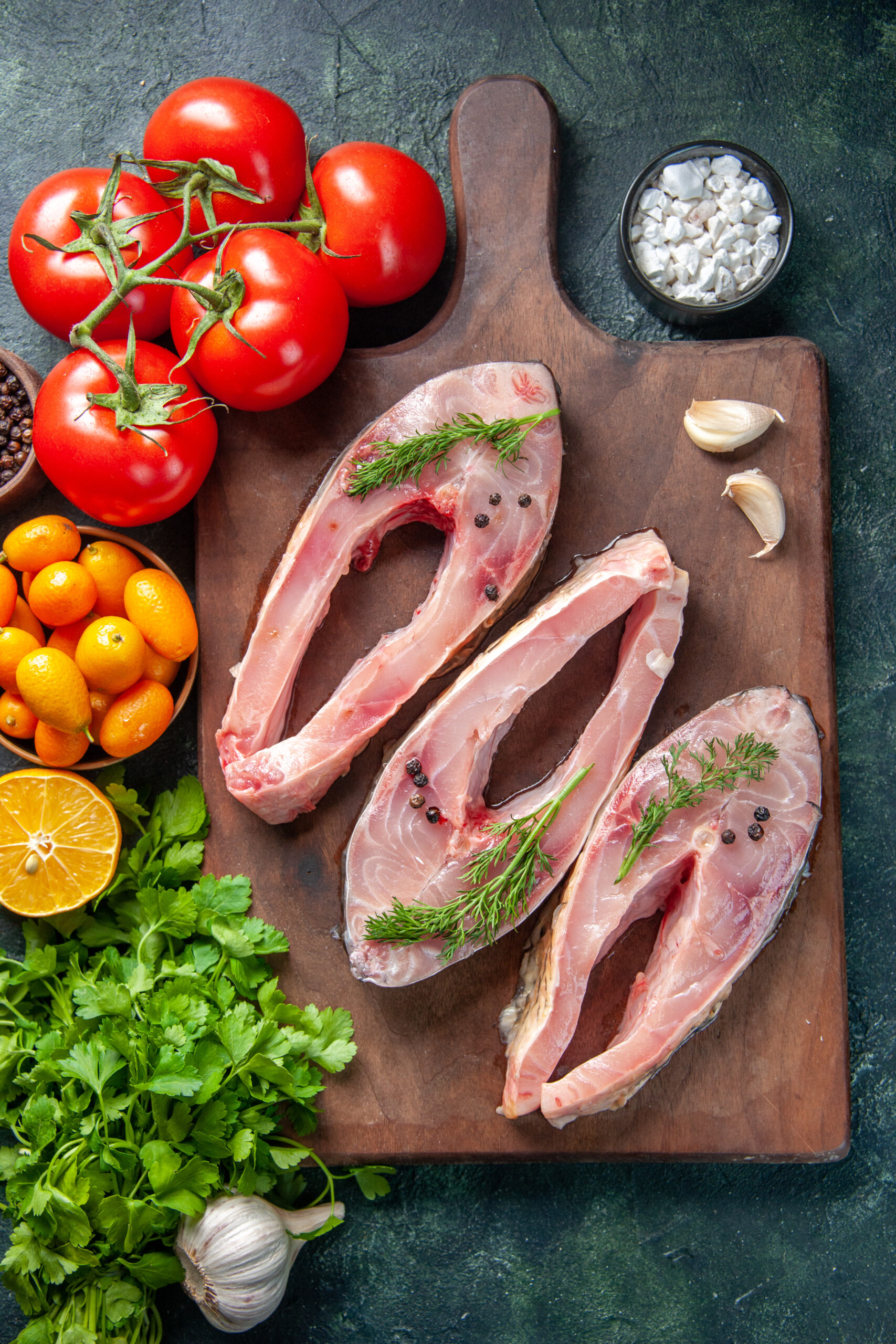 About top view fresh fish slices with greens kumquats dark background